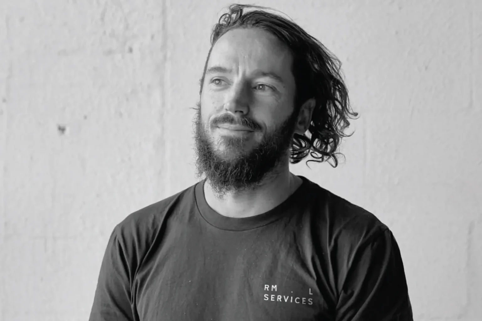 RML Services branded t-shirt worn by a bearded man, black and white portrait against a pale wall