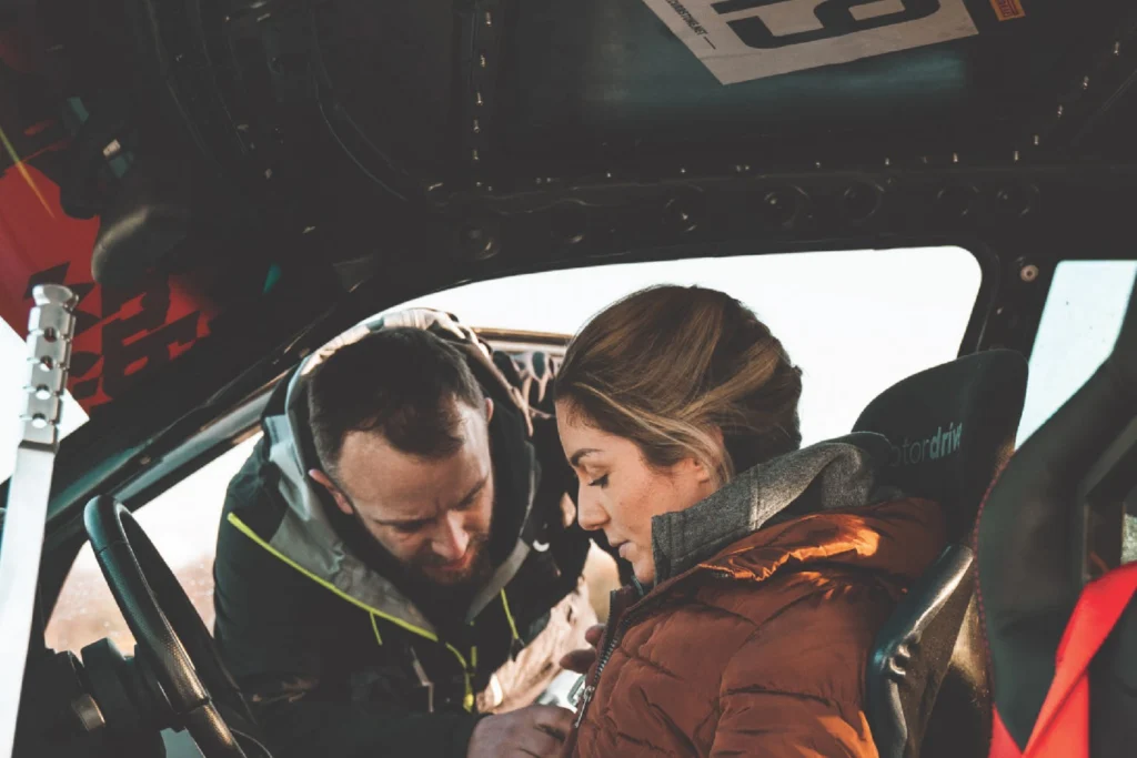 Sportech Motorsport: a man leans into a rally car to help a participant in a bucket seat with her harness