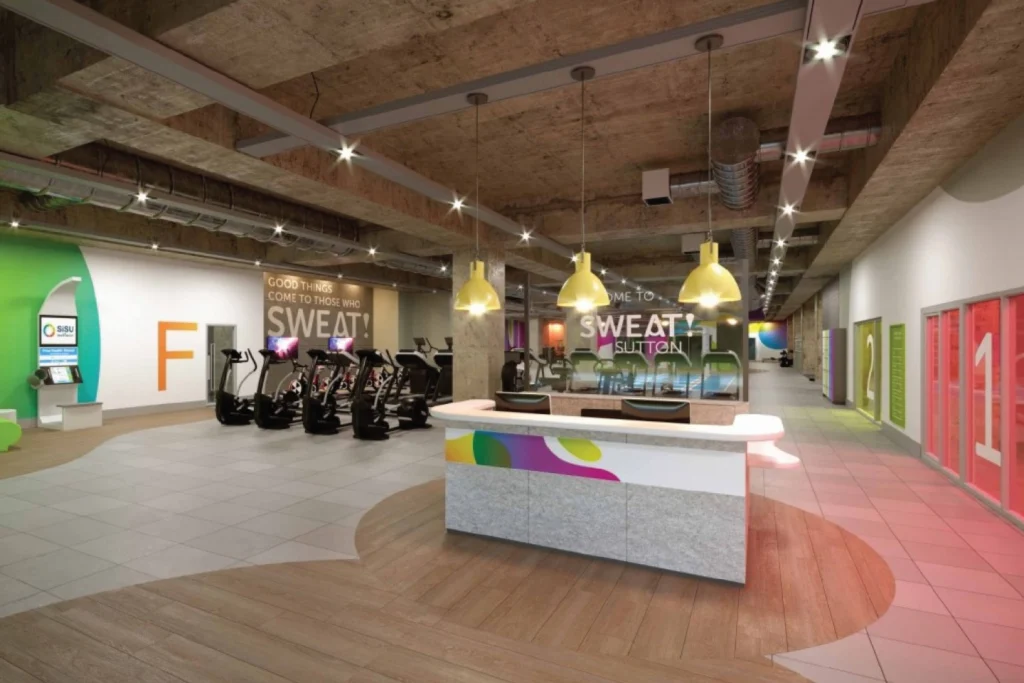 Rendered visualisation of the Sweat! Gym reception and gym floor, with yellow pendant lights, branded signage and bikes
