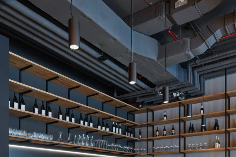 The Mad Ox interior: back bar shelves of wine bottles and glassware under cylinder pendant lights and exposed ducts