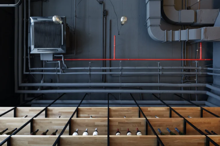 The Mad Ox interior: timber wine racks below grey-painted pipework, ducting and a red sprinkler pipe