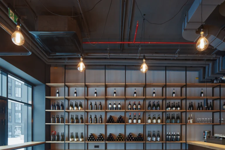 The Mad Ox interior: wine bottles on open timber and steel shelving under filament pendants and exposed ductwork