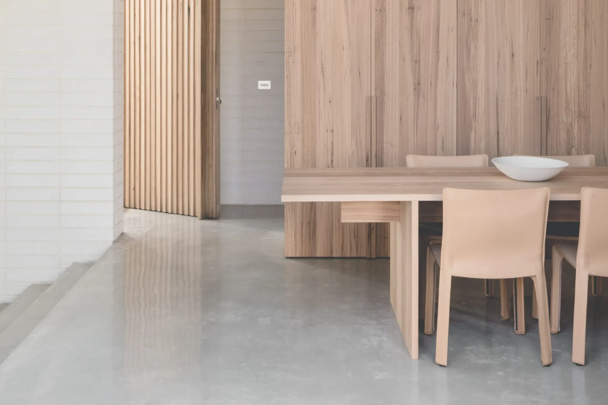 Williams Joinery photography: timber dining table and full-height cabinetry beside a slatted screen on a concrete floor