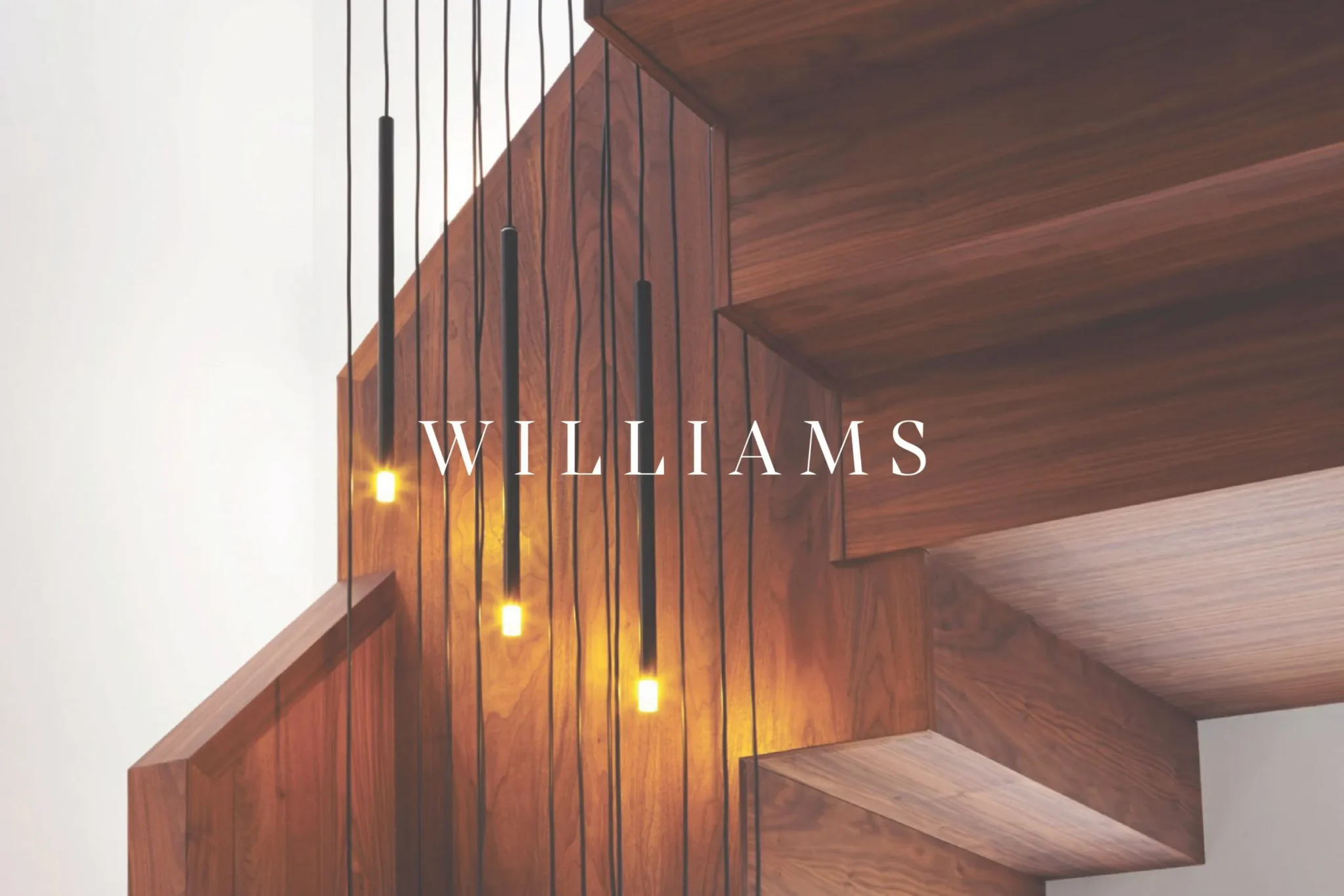 Williams Joinery serif wordmark over a dark timber staircase lit by slim black pendant lights